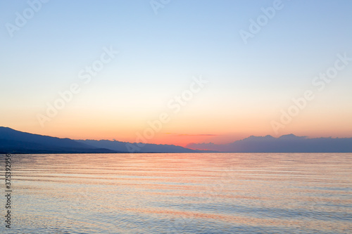 Dawn of the sun at sea. The rising sun behind the mountains. Kyrgyzstan.