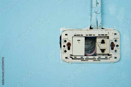 Power switch and defective plug, dirty and dangerous, No maintenance electric plug, on blue pastel wall.