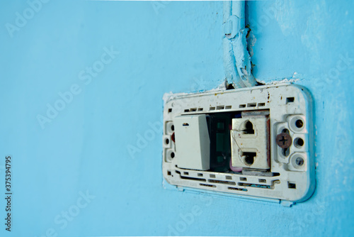 Power switch and defective plug, dirty and dangerous, No maintenance electric plug, on blue pastel wall.