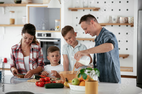 Mother and father making breakfast with sons. Young family preparing delicious food in kitchen..