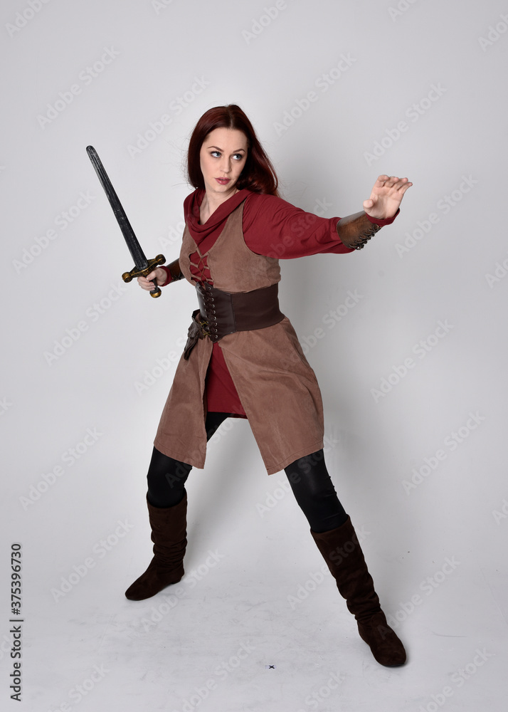 Full length portrait of girl wearing medieval costume. Standing pose holding a sword, isolated against a grey studio background. Full length portrait of girl wearing medieval costume. Standing pose holding a sword, isolated against a grey studio background.