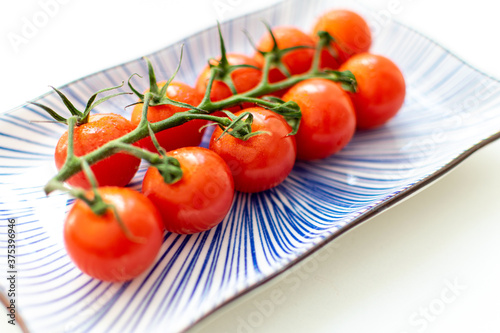 a macro image of a cut vine of cherry tomatoes presented on a blue ceramic plate © josehidalgo87