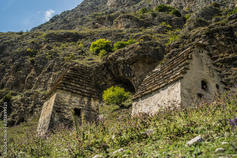 Ancient stone houses in green mountains. Amazing landscape with aged stone buildings located on green grassy slope of rocky mountain in sunny summer day Ancient stone houses in green mountains. Amazing landscape with aged stone buildings located on green grassy slope of rocky mountain in sunny summer day