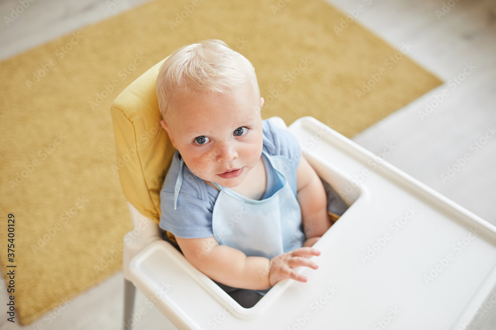 From above view shot of little toddler wearing bib sitting on high chair waiting for meal, copy space From above view shot of little toddler wearing bib sitting on high chair waiting for meal, copy space