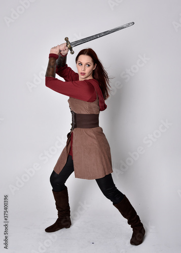 Full length portrait of girl wearing medieval costume. Standing pose holding a sword,  isolated against a grey studio background. photo