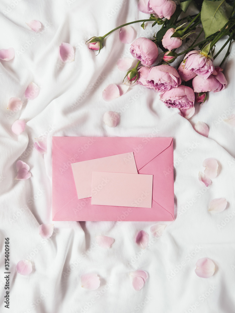 Roses and petals on crumpled white fabric. Natural elegant decoration. Romantic background with copy space on pink envelope and visit cards. Top view, flat lay. Roses and petals on crumpled white fabric. Natural elegant decoration. Romantic background with copy space on pink envelope and visit cards. Top view, flat lay.