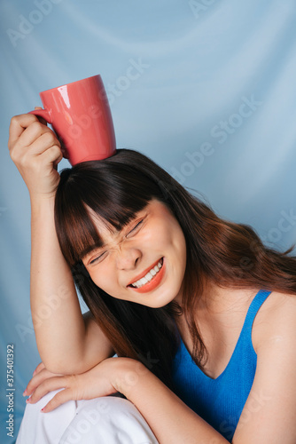 Cheerful young asian dark hair woman holding a cup of coffee over head.