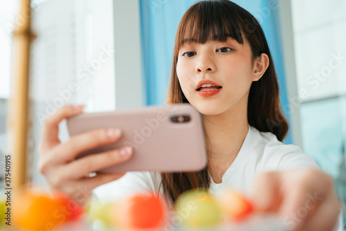 Portrait of young asian dark hair woman taking photo of pastel fruit shaped mung bean. © THESHOTS.CO