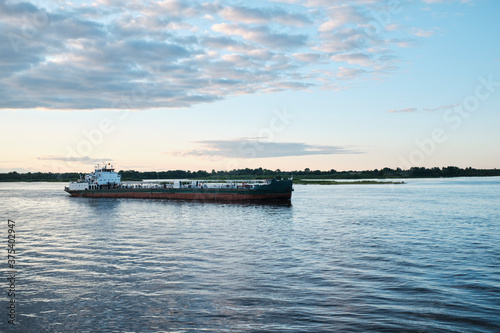 cargo ship floating on the river in the rays of the setting sun