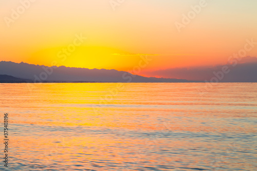 Dawn of the sun at sea. The rising sun behind the mountains. Kyrgyzstan.