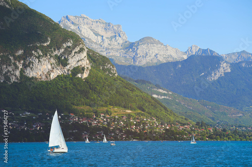 View of Annecy lake with clear turquoise water, sailing boats and traditional wooden houses in summer day, France
