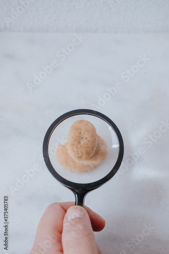 close up of hand holding a magnifying glass and watching wholegrain cookie on the white marble table photo