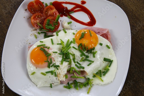 Top view on fried eggs on brad with jam, tomatoes and green fresh chives