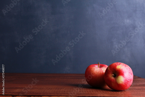 Two red fresh apples on brown wooden table against dark blue wall background with copy space. Natural organic food, healthy eating, harvest season concept