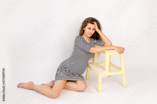 a beautiful pregnant girl in a striped dress sits on a white isolated background, a place for text