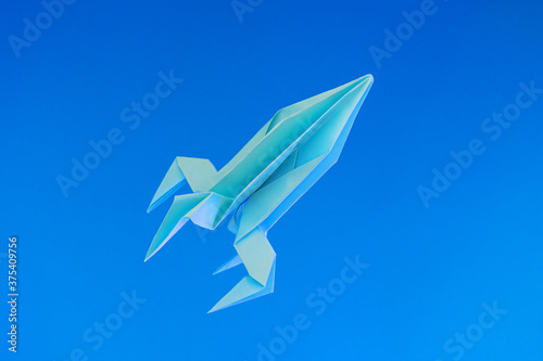 Paper origami rocket flies on a blue background. Space concept. International Day of Human Space Flight, Cosmonautics Day.