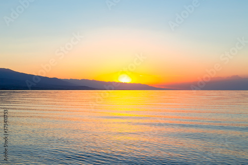 Dawn of the sun at sea. The rising sun behind the mountains. Kyrgyzstan.