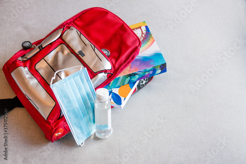 A red bagpack of a kid with a blue disposable mask and hand sanitizer set ready for back to school photo