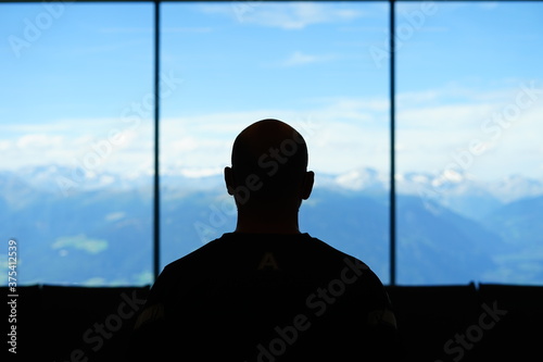 Silouette of a bald man watching the mountain from the window of an alpine refuge photo