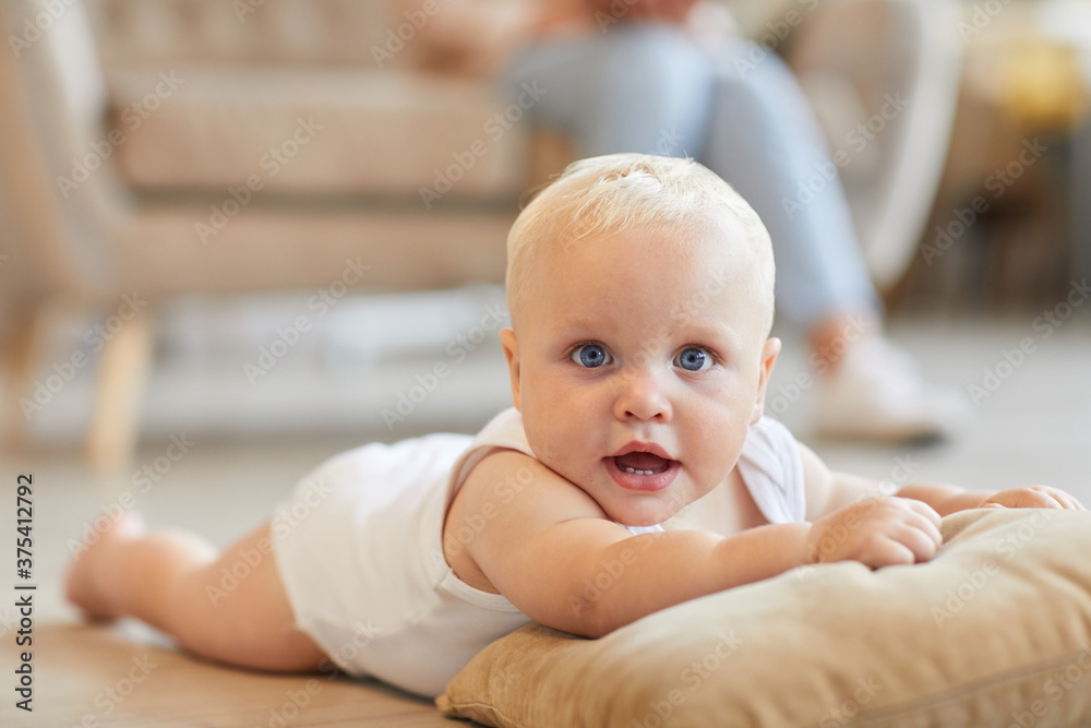 Horizontal medium close-up shot of playful baby having fun on floor lying on pillow while his mom sitting on sofa Horizontal medium close-up shot of playful baby having fun on floor lying on pillow while his mom sitting on sofa