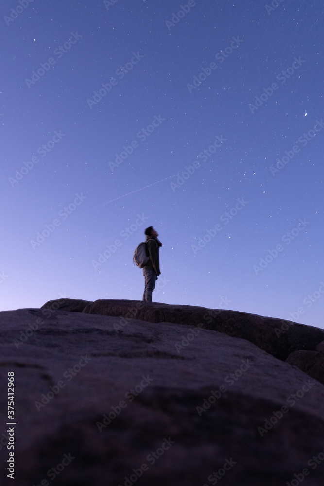 Young hiker watching shooting star pass by on top of mountain in the early morning before sunrise