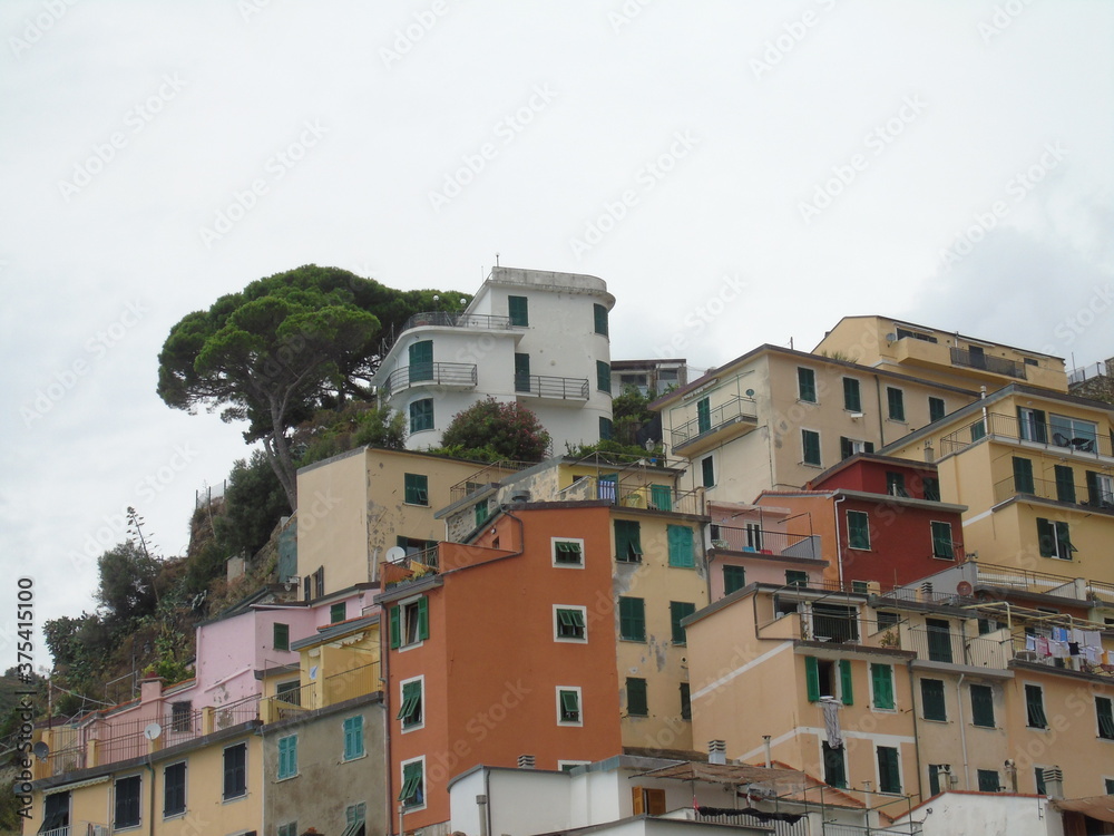 Riomaggiore, Italy - 08/31/2020: Beautiful photography of the countryside from Cinque Terre, Italy. Grey sky, colourful houses, grape coltivation from the mountains, and some small waves from the sea.