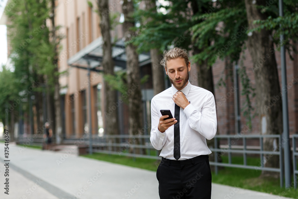 Portrait of a successful young businessman. A curly-haired man in a white shirt with a telephone against the background of a modern business center. Portrait of a successful young businessman. A curly-haired man in a white shirt with a telephone against the background of a modern business center.