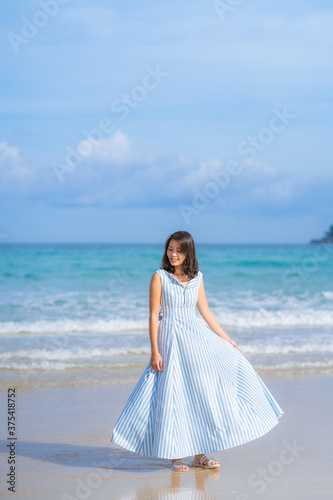 Full length of happy woman in beautiful blue summer dress posing and enjoying a walk on the sea beach with blue sky horizon, vacation and travel ocean concept. Phuket, Thailand.