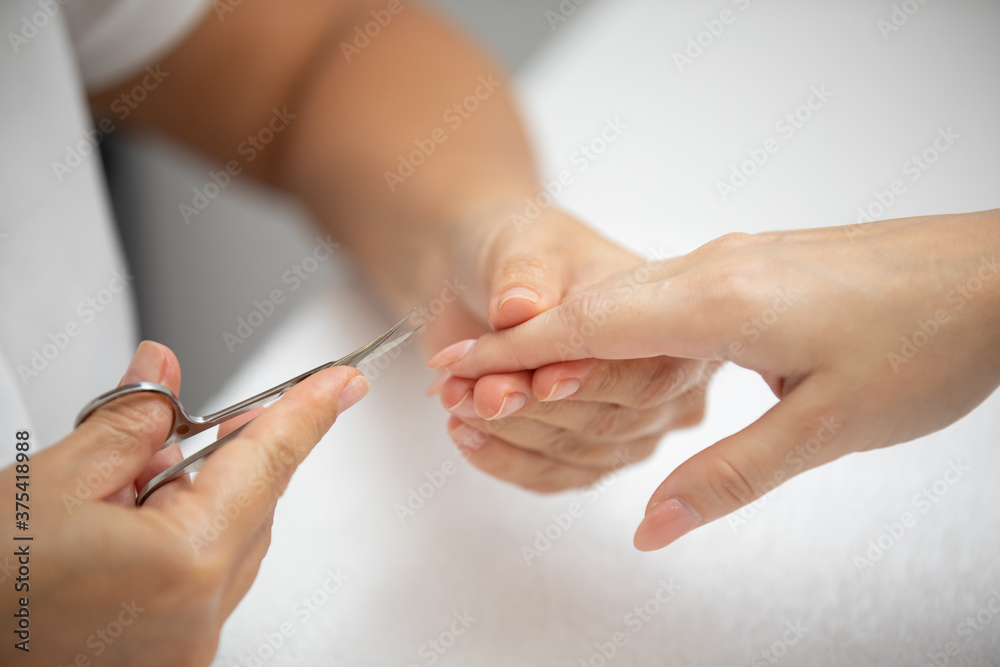 Close up of manicurist hands clipping client nails in a luxury spa. Young woman getting manicure treatment with hands kept on towel. Clipping nails, hand care and nailcare at beauty salon. Close up of manicurist hands clipping client nails in a luxury spa. Young woman getting manicure treatment with hands kept on towel. Clipping nails, hand care and nailcare at beauty salon.