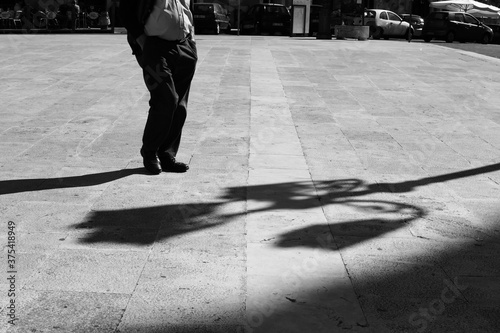 Sicilian man in a square with his hands in his pockets with elongated shadow in black and white.Black and white. Shadow and light, man silhouette