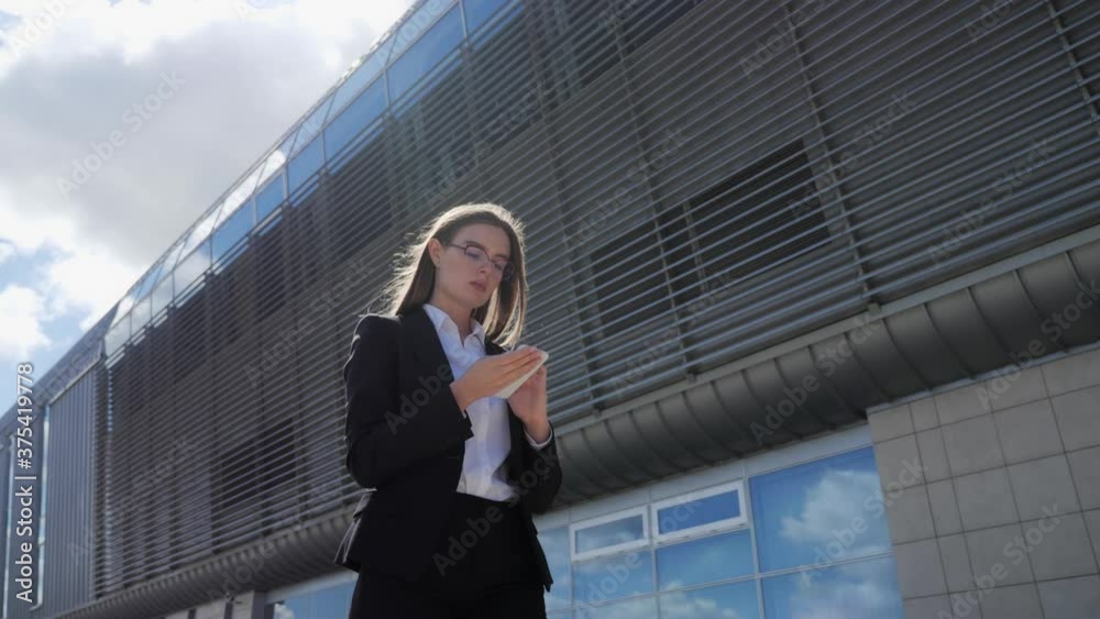 Attractive business woman walking on the background of a modern building and typing a message bottom view. Attractive business woman walking on the background of a modern building and typing a message bottom view.