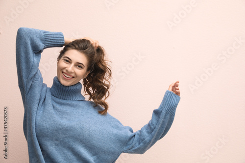 Beautiful young woman wearing warm blue sweater on light pink background