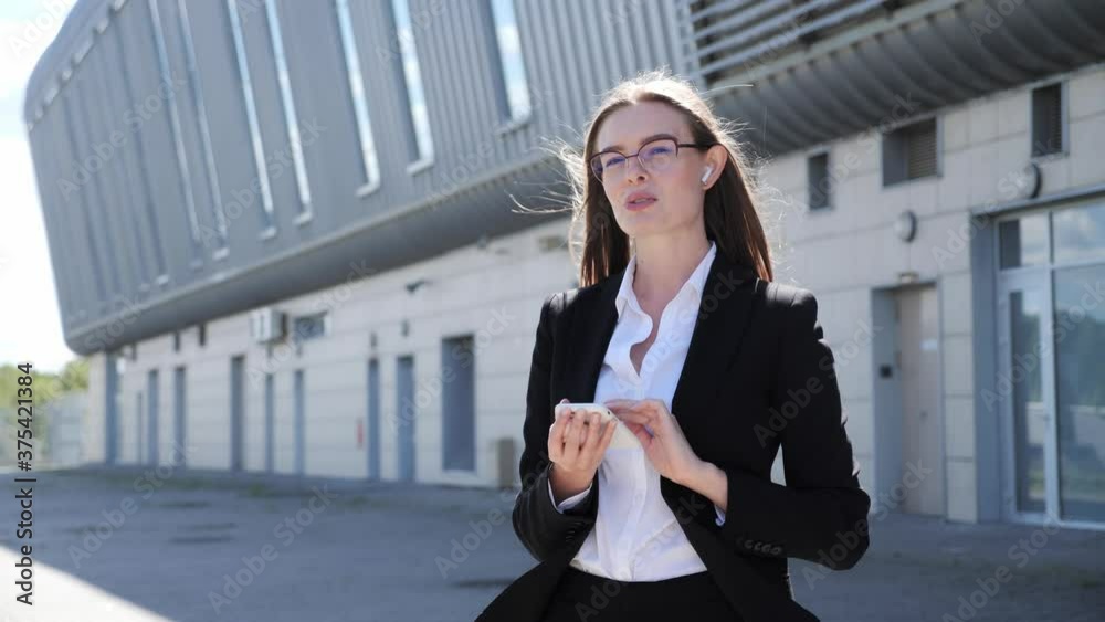 Elegant businesswoman talking on smartphone using wireless headphones on the background of business center. Elegant businesswoman talking on smartphone using wireless headphones on the background of business center.