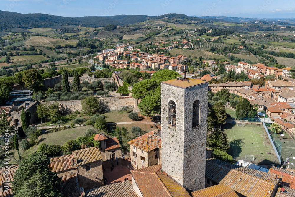 Aerial view of medieval tower, houses and modern sports grounds in San Gimignano, Italy, and the surrounding fields, forests and mountains