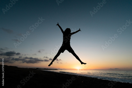 A girl jumps for joy on the beach at dawn. Concept of happiness
