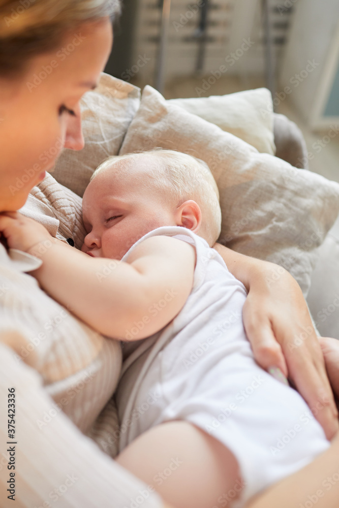 Vertical high angle shot of young Caucasian mother sitting on sofa cuddling her baby son in arms Vertical high angle shot of young Caucasian mother sitting on sofa cuddling her baby son in arms
