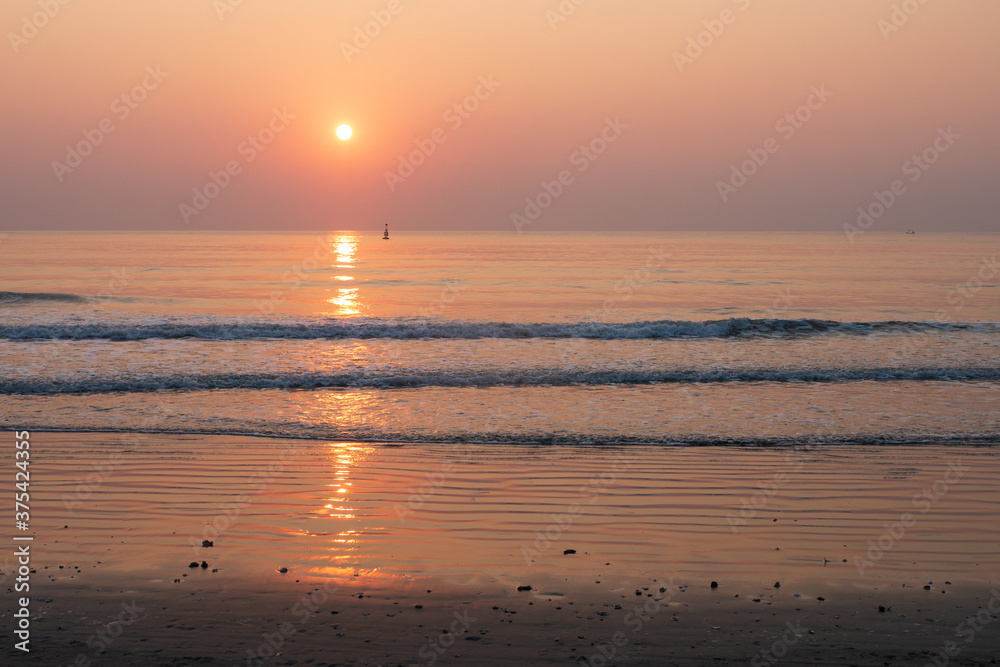 Nature background of seashore beach wave and coastline sand with sunset on water surface for holiday relaxation lifestyle concept