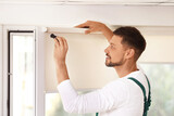 Handyman with screwdriver installing roller window blind indoors