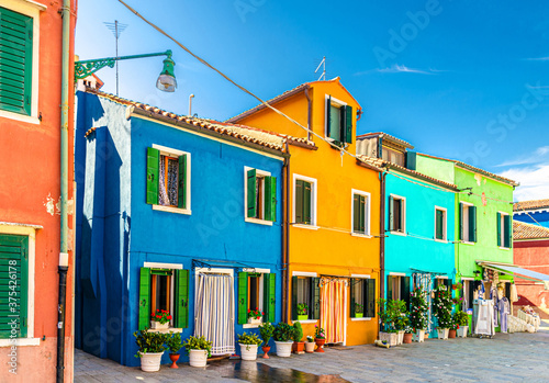 Burano island colorful houses with multicolored walls, striped curtain on doors, shutter windows and flowers in pot, sunny summer day, Venice Province, Veneto Region, Northern Italy. Burano postcard