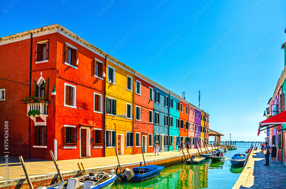 Burano island with colorful houses and buildings on embankment of narrow water canal with fishing boats and view of Venetian Lagoon, Province of Venice, Veneto Region, Northern Italy. Burano postcard