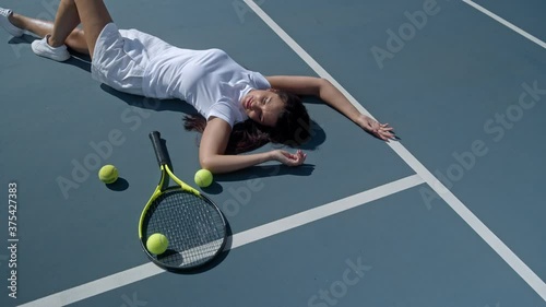 Tired depressed young female tennis player lies on outdoor tennis court with a lot of balls after hard training at sunset. Top view. Motivational video, power and result