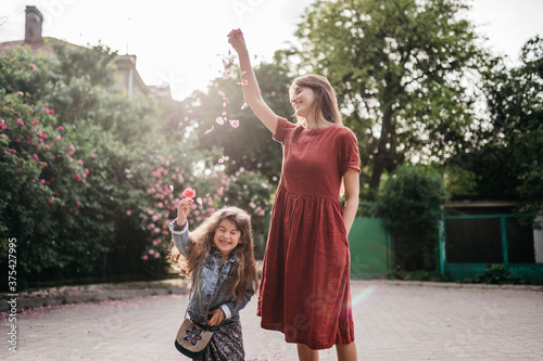 happy mom and cheerful daughter play with rose petals in the park 