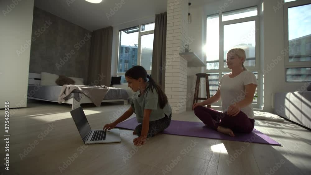 Happy healthy family kid daughter and young mother having fun doing yoga exercises together, smiling mindful mom teaching little cute child girl to meditate laughing at home Happy healthy family kid daughter and young mother having fun doing yoga exercises together, smiling mindful mom teaching little cute child girl to meditate laughing at home