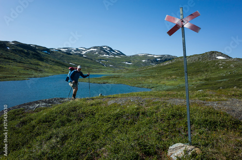 Hiking in Swedish Lapland. Man traveler trekking alone with view of mountain lake Allagasjavri in northern Sweden. Arctic nature of Scandinavia in warm summer sunny day with blue sky photo