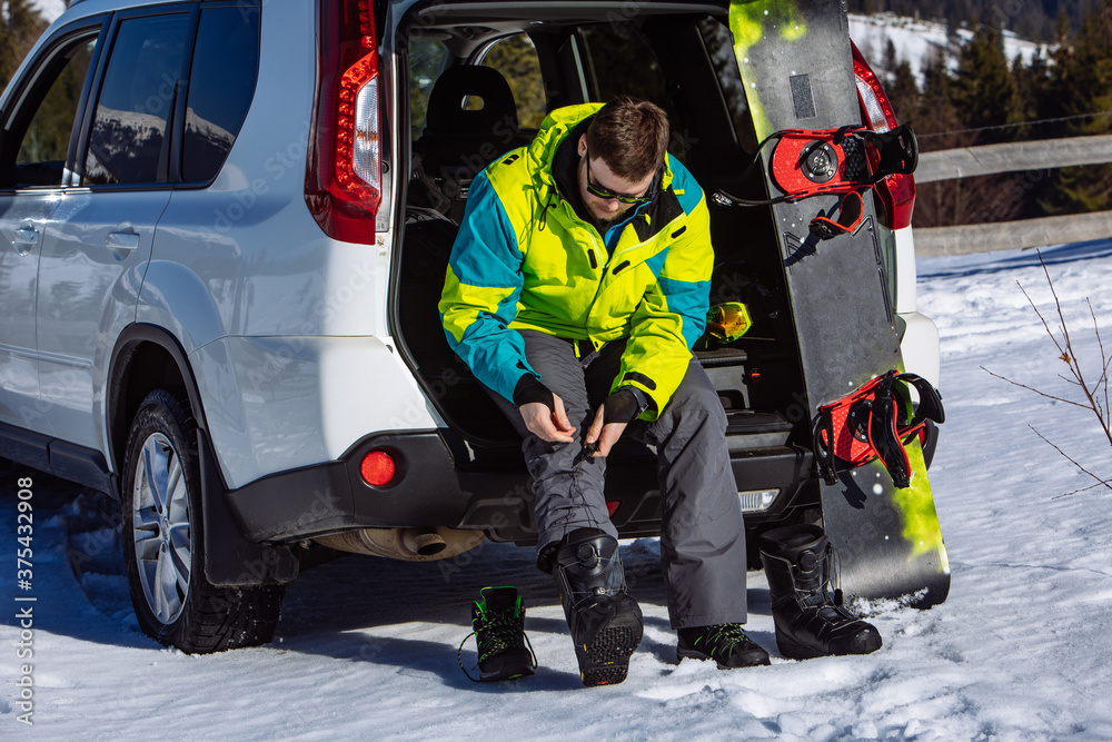 man sitting in car trunk changing for snowboard man sitting in car trunk changing for snowboard