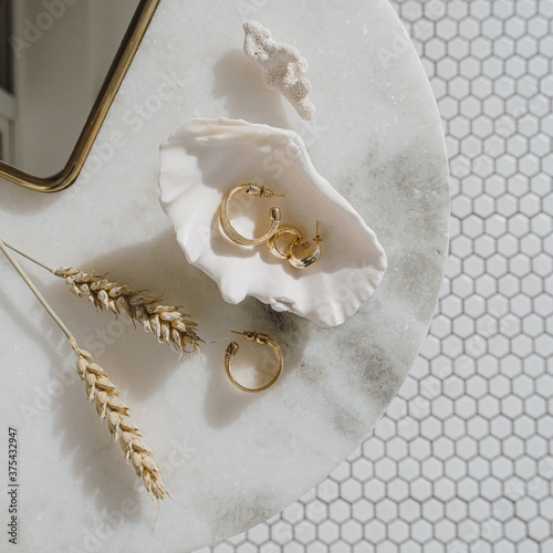 Minimal fashion composition with golden earrings in seashell on marble table with mirror and wheat stalks. Flat lay, top view bijouterie / jewelry concept on mosaic tile background. photo