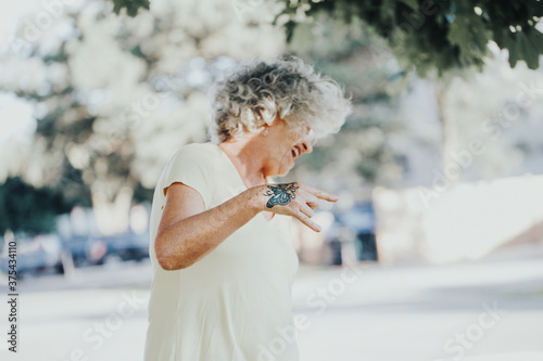 Cool edgy Caucasian old lady woman with butterfly tattoo on hand. Beautiful funky elderly woman with grey hair making devil rock sign with fingers. Young at heart senior person. photo