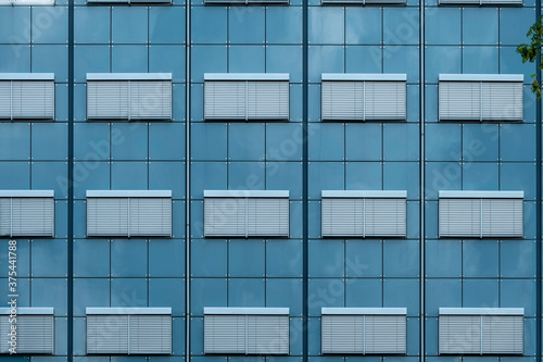 Abstract view of a build face with closed windows and blue glass wall under a hash summer sun light