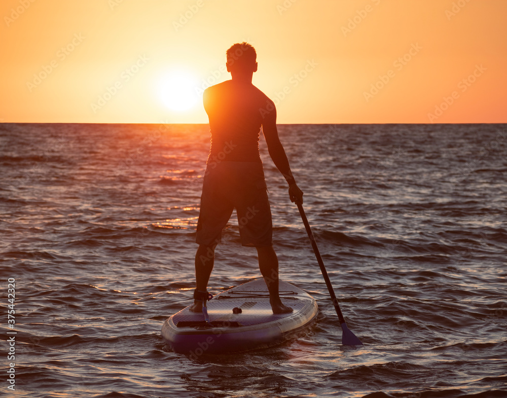 Silhouette of active man standing with paddle on SUP at sunset background