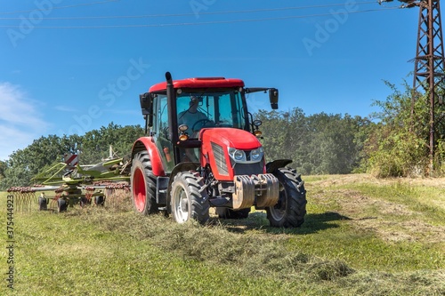 Modern red tractor in the agricultural field. Work on an organic farm. Haymaking. Tractor on a green field.